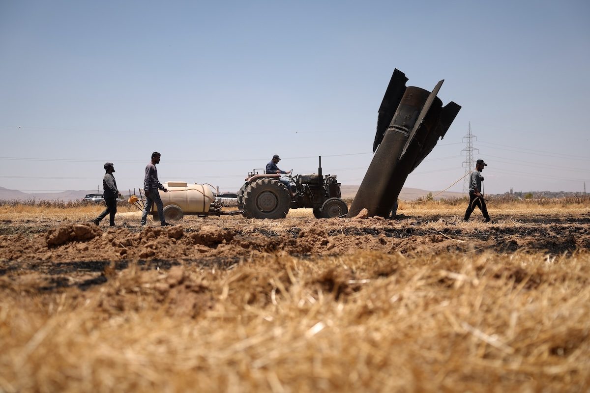 Parte di un missile iraniano in un campo in Siria, con un trattore all'orizzonte